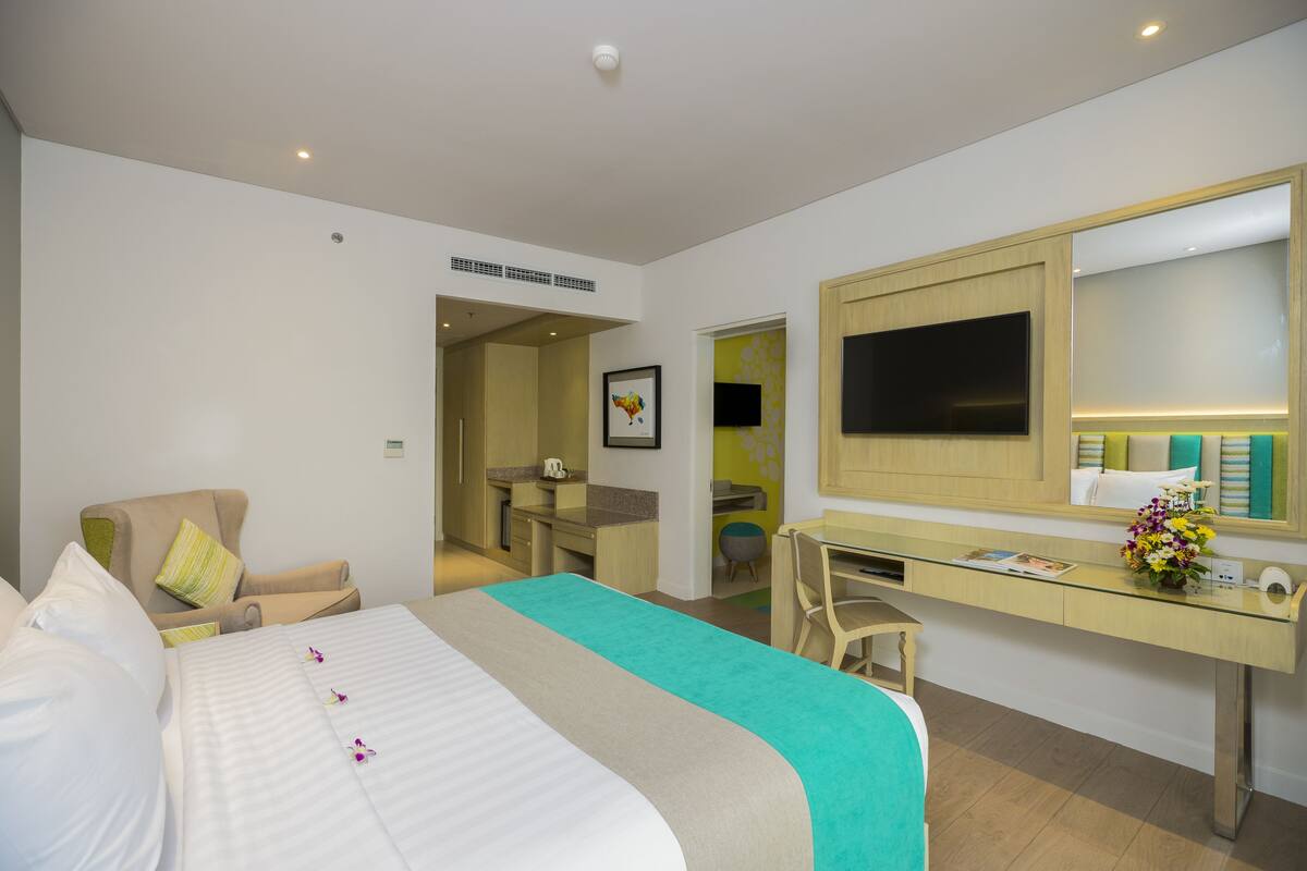 Une chambre d’hôtel avec un lit, un bureau, une chaise, une télévision et une salle de bain visible à travers une porte ouverte.