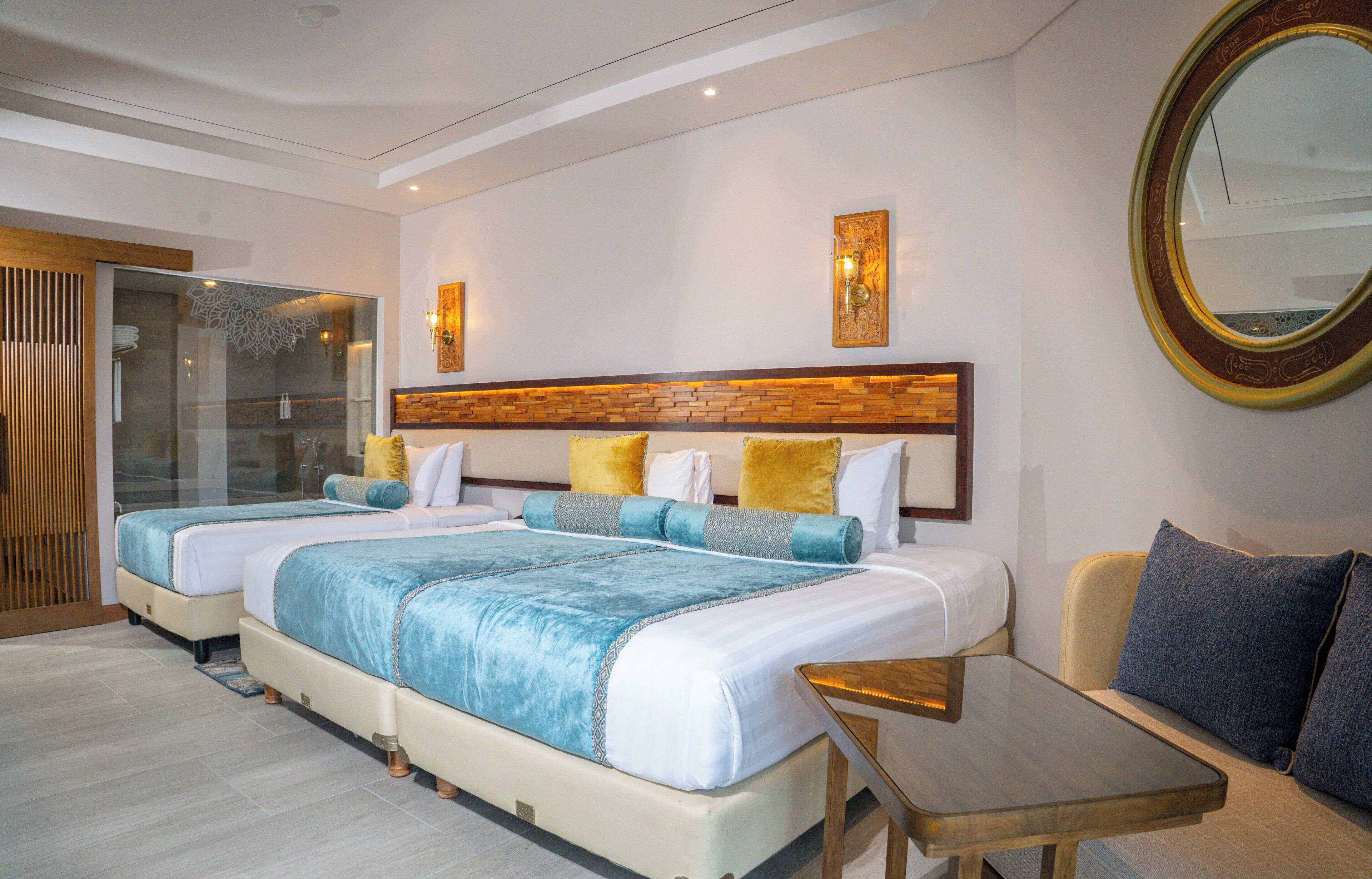 A hotel room with two beds, a sofa, a glass shower enclosure, and a large mirror.