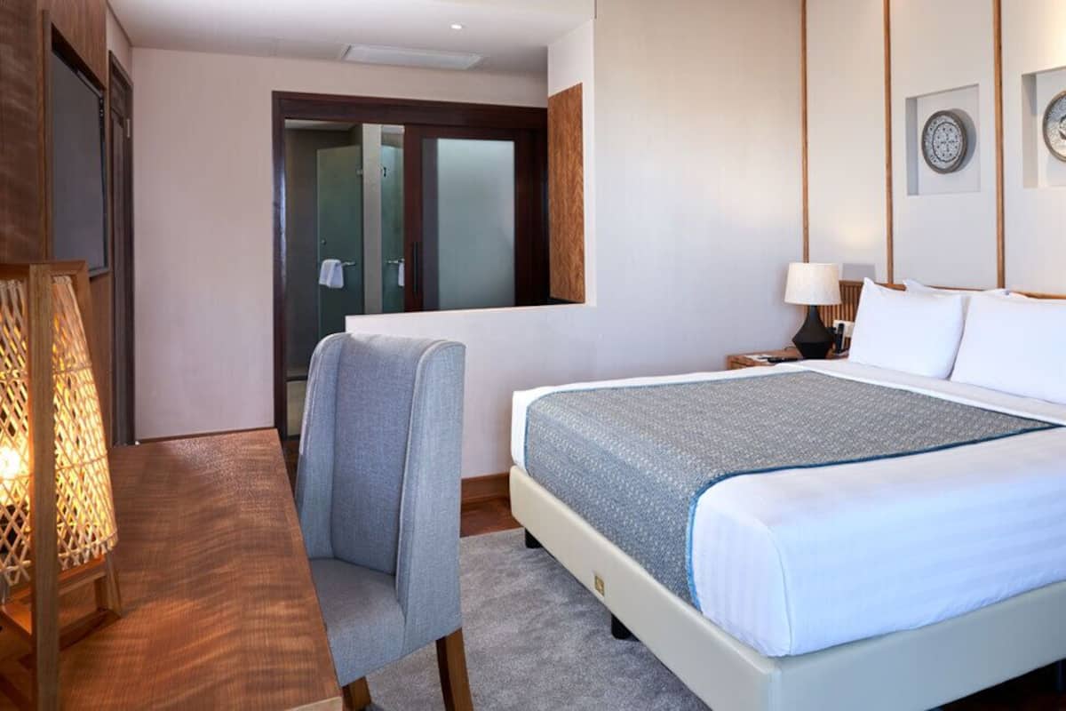 Une chambre d’hôtel comprenant un lit, des tables de chevet, une chaise et des œuvres d’art décoratives au mur.