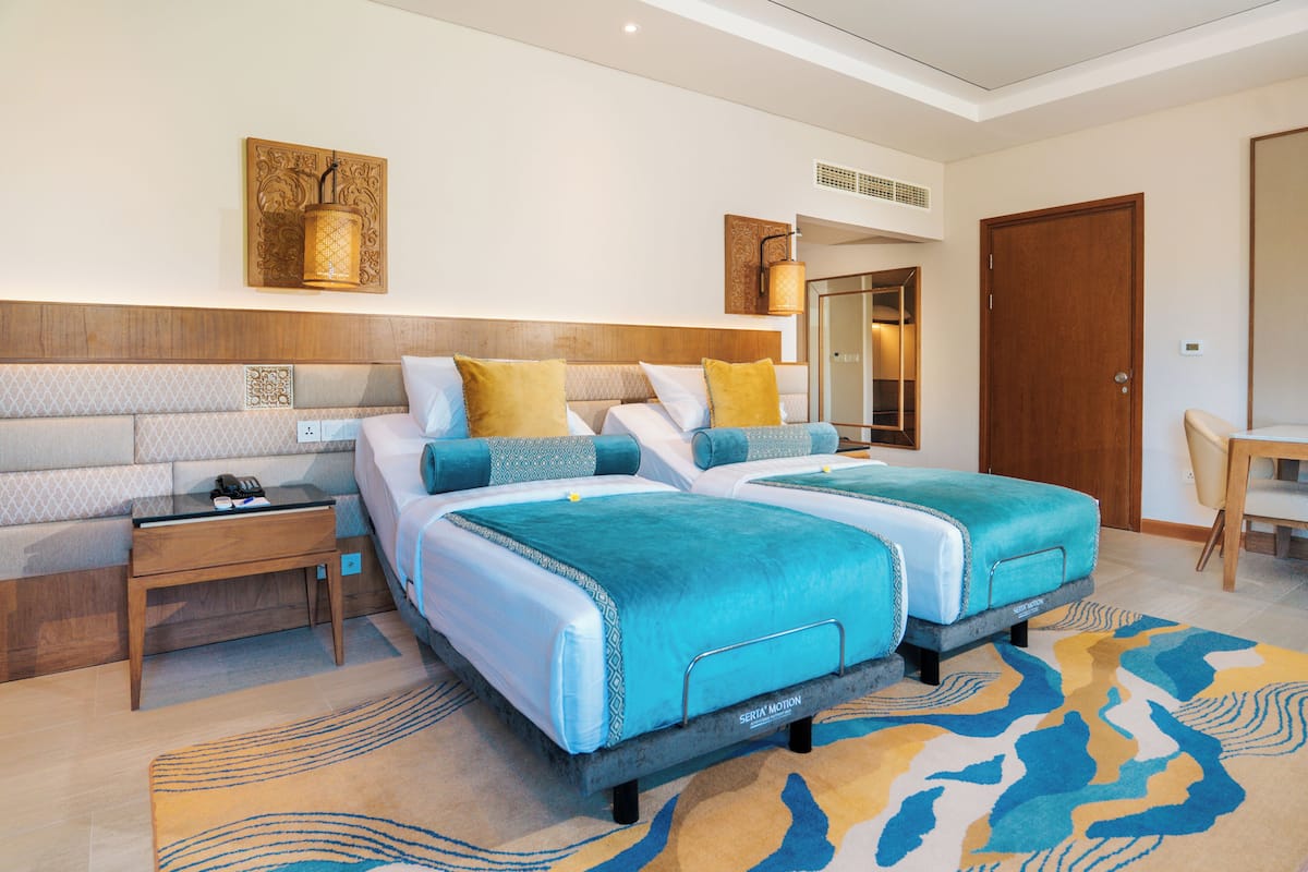Une chambre d’hôtel avec deux lits, une table de chevet, un bureau, une chaise et un grand miroir.