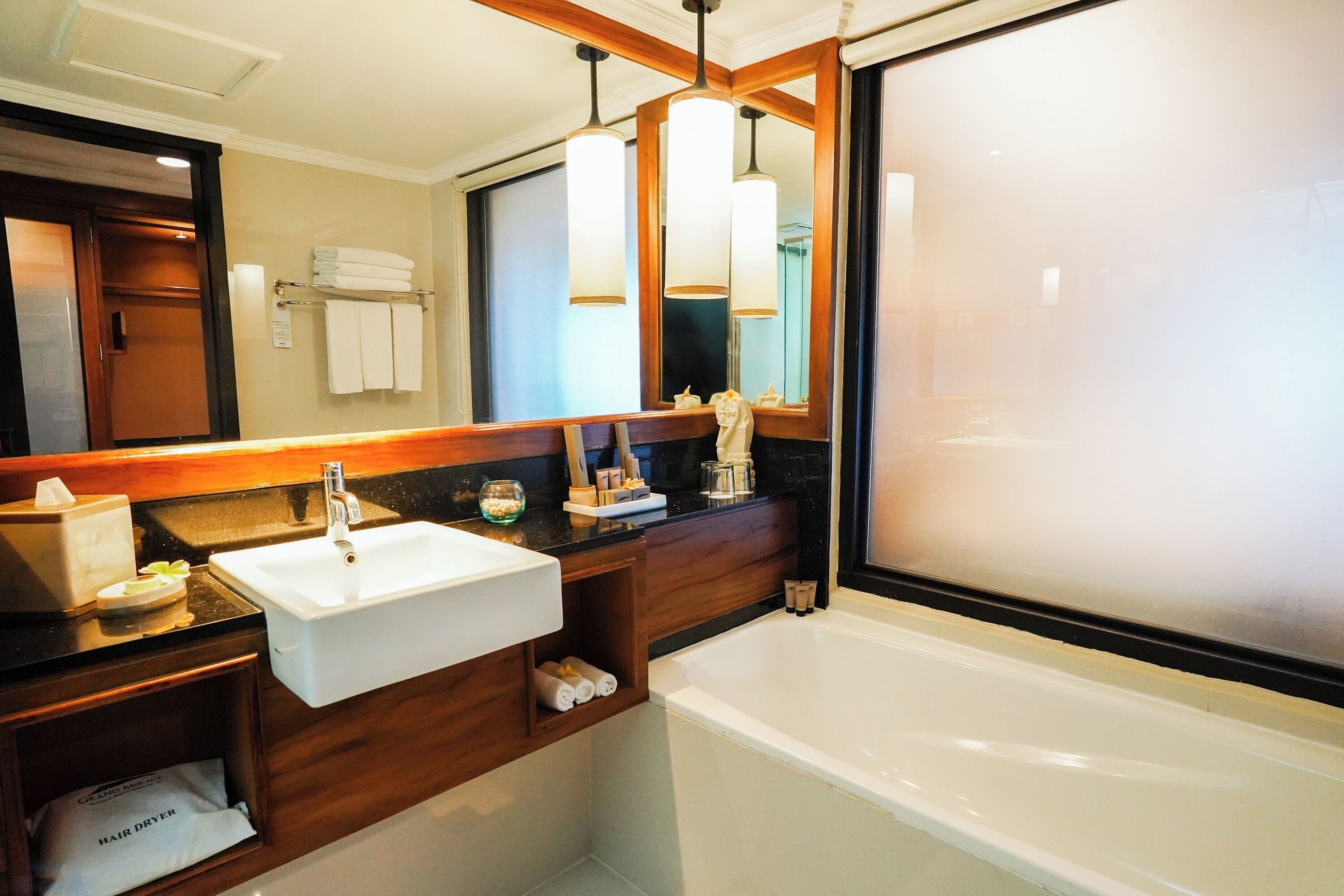 A modern bathroom with a white sink, vanity, and bathtub. There are towels and toiletries on the counter, and a large mirror above the sink.