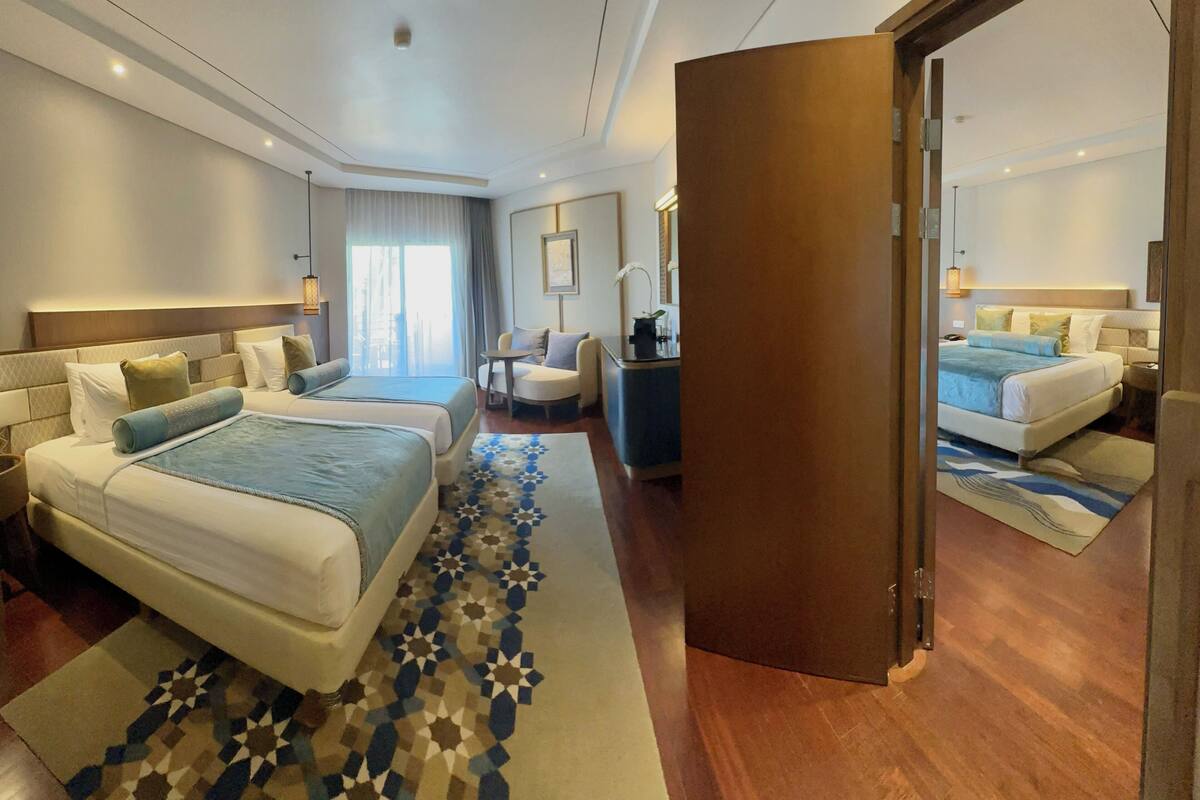 Une chambre d’hôtel avec deux lits, un coin salon avec une chaise et une table, et un grand miroir.