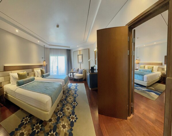 Ein modernes Hotelzimmer mit einem großen Bett, einem Einzelbett, einem Schreibtisch und einer Sitzecke.