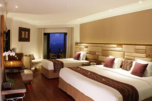Ein Hotelzimmer mit zwei Betten, einem Schlafsofa, einem Schreibtisch und Meerblick.