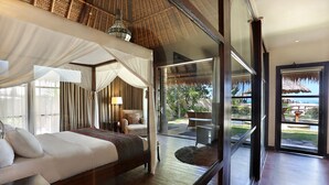 Ein geräumiges Schlafzimmer mit einem großen Bett, einer Sitzecke mit einem Sessel und Blick ins Freie durch eine Glastür.