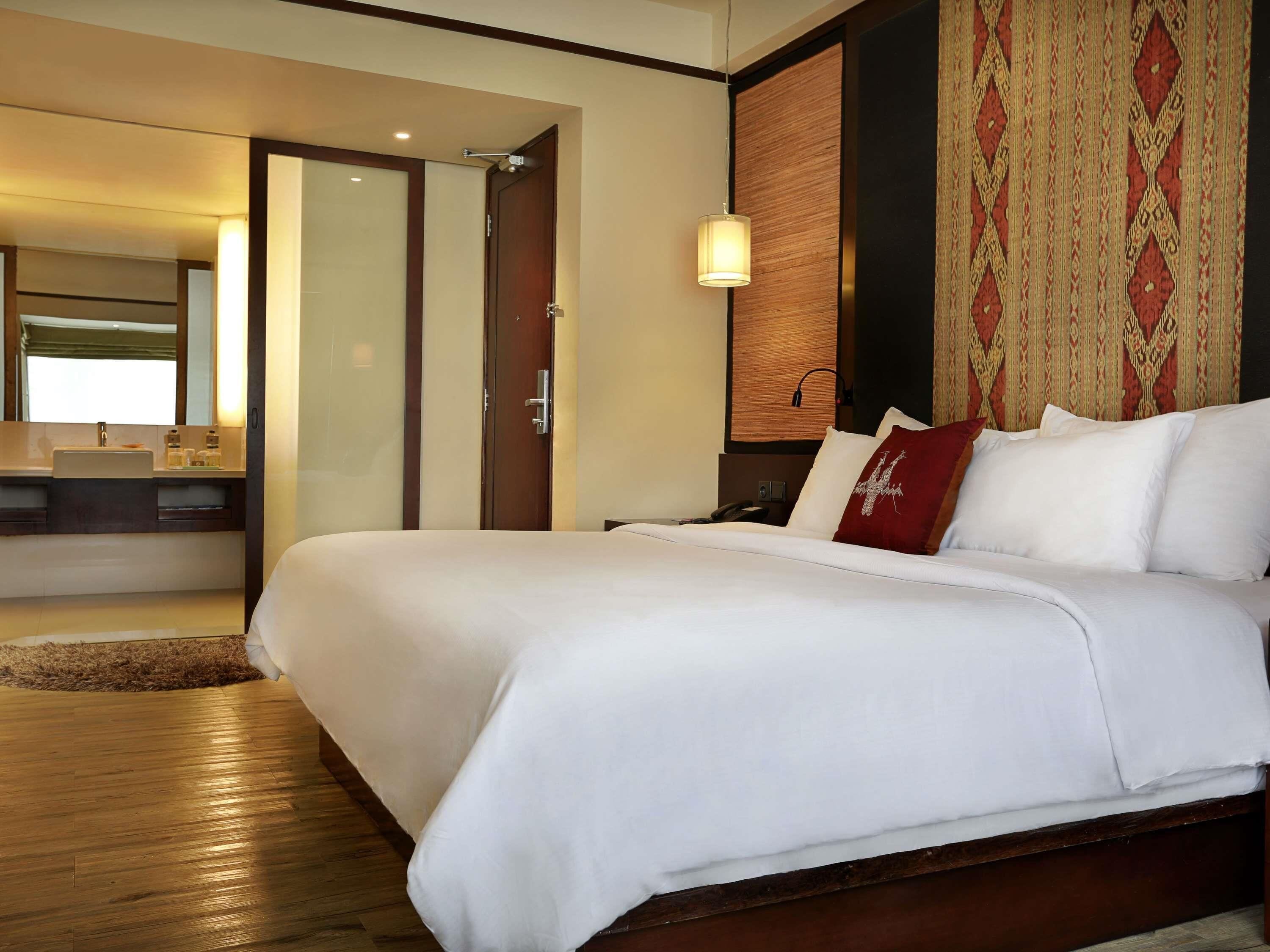 A hotel room with a large bed, a wooden floor, a bathroom with a sink and mirror, and a patterned wall.