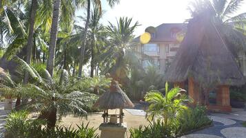 A resort courtyard with palm trees, a thatched-roof structure, and a building in the background.