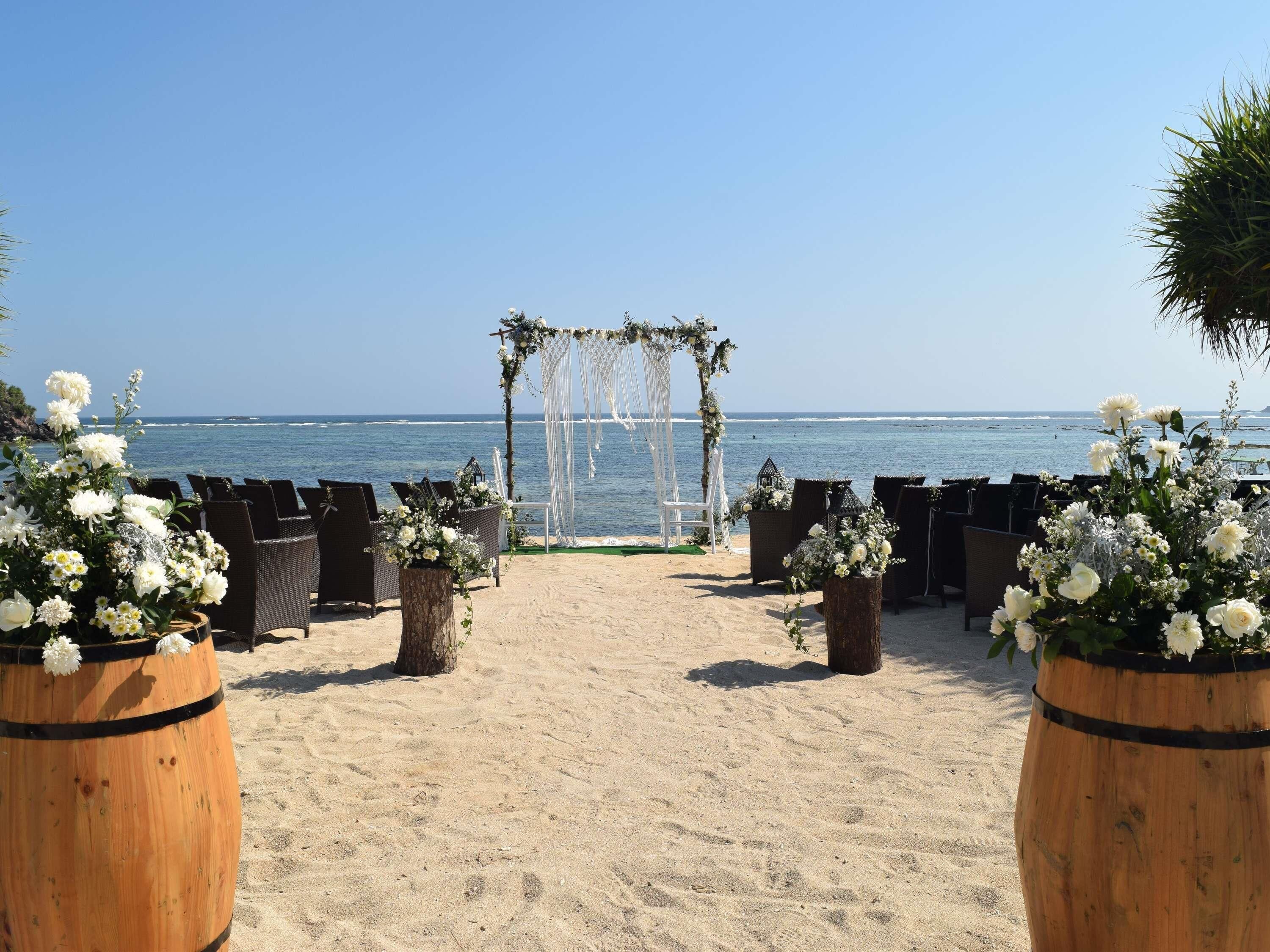 Een bruiloftdecoratie op het strand, met een bloemrijke boog, stoelen en potplanten.