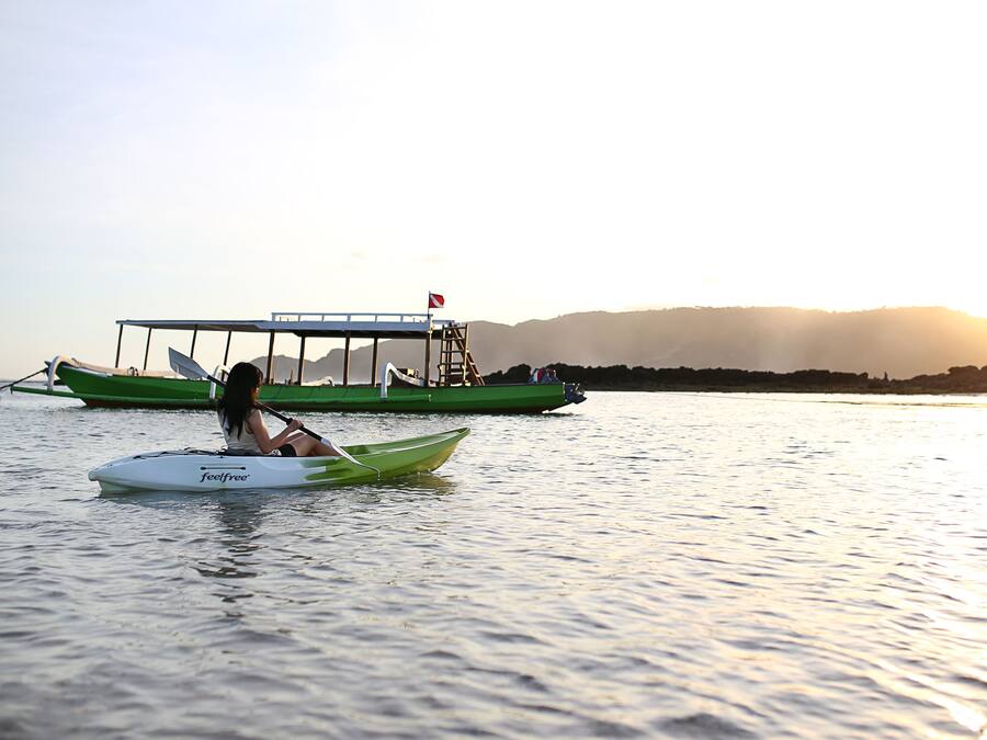 Una persona en un kayak verde sobre aguas tranquilas, con un bote verde amarrado al fondo.