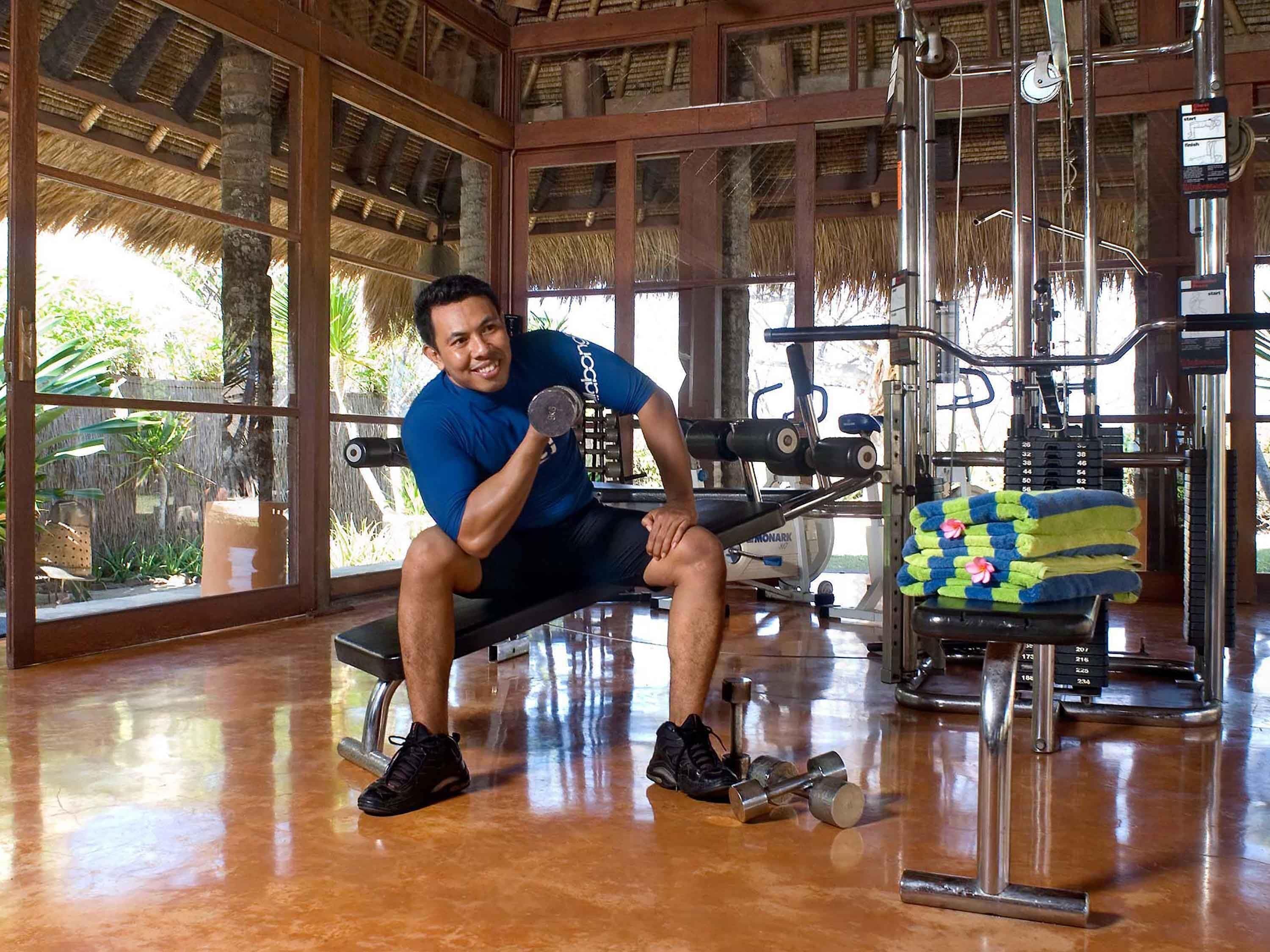 A man sitting on a bench in a gym with exercise equipment and a large window.