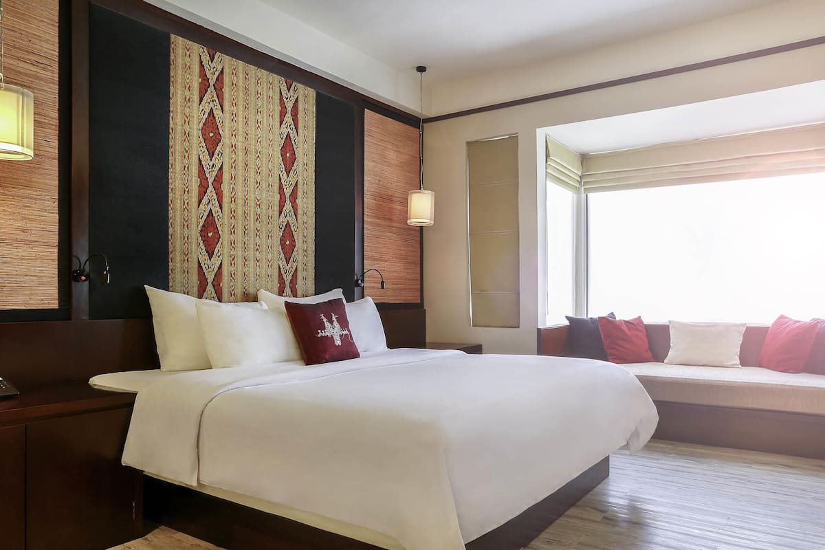 A hotel room with a large bed, bedside tables, a patterned wall hanging, and a window with curtains.
