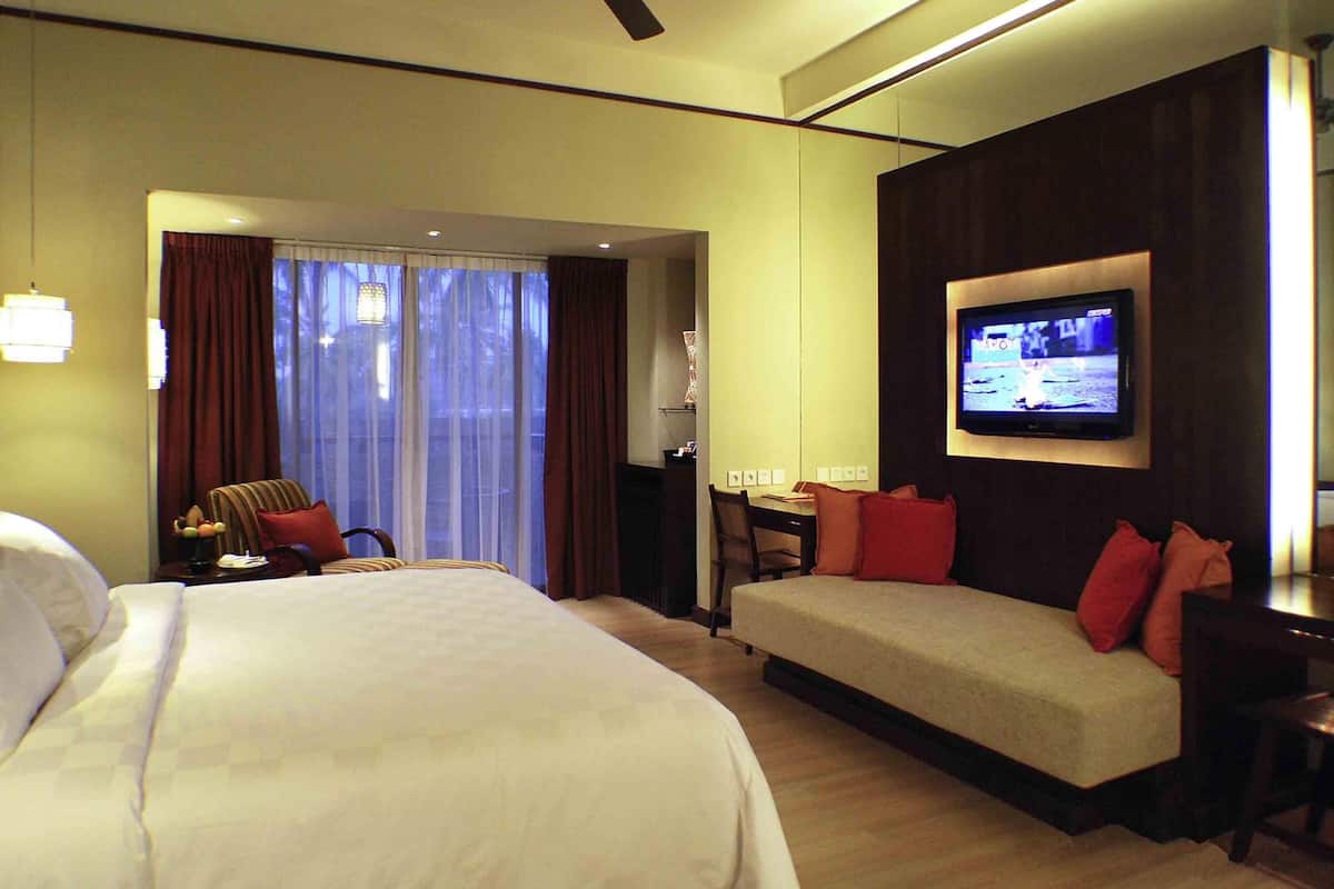A hotel room with a bed, a sofa, a TV, and a ceiling fan.