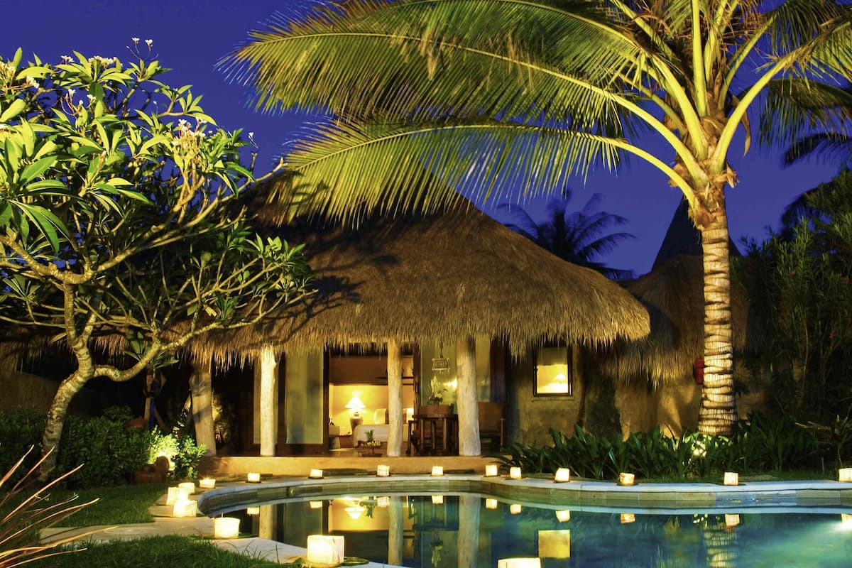 A thatched-roof building with a pool and candles.