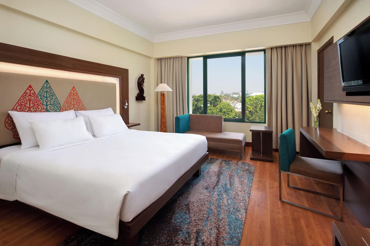A hotel room with a large bed, a desk, a chair, a TV, and a window with a view.