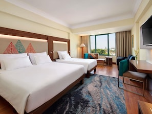 A hotel room with two beds, a desk, a chair, a TV, and a large window with a view. - Novotel Solo (Surakarta)