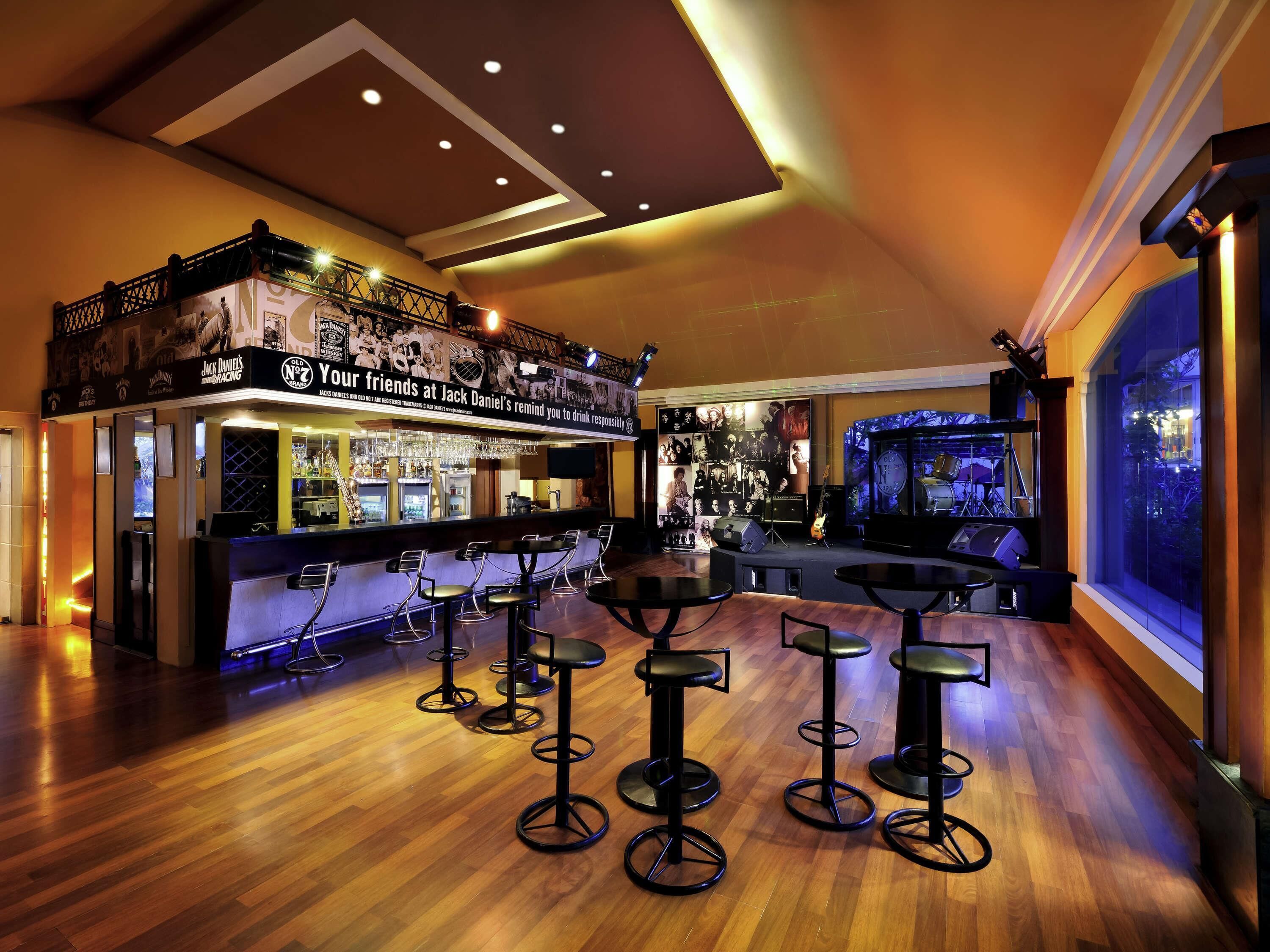A bar area with stools, a stage with musical instruments, and a large window.