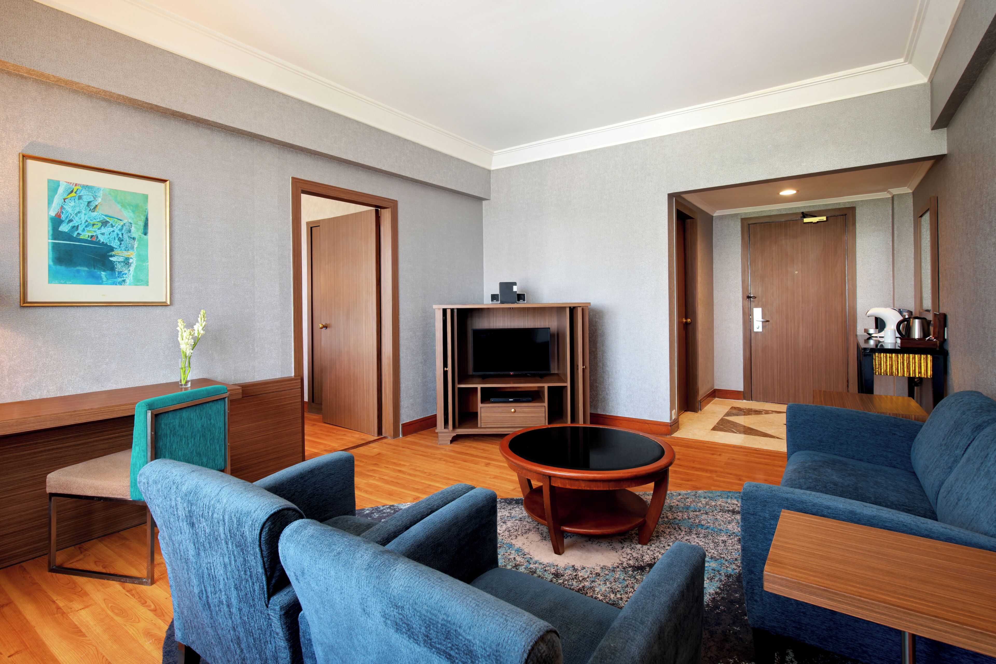 Een moderne woonkamer met een flatscreen televisie, twee blauwe banken, een salontafel en een ingelijst kunstwerk aan de muur.