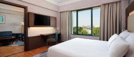 Habitación de hotel con una cama grande, un escritorio, un televisor y vista a la ciudad.