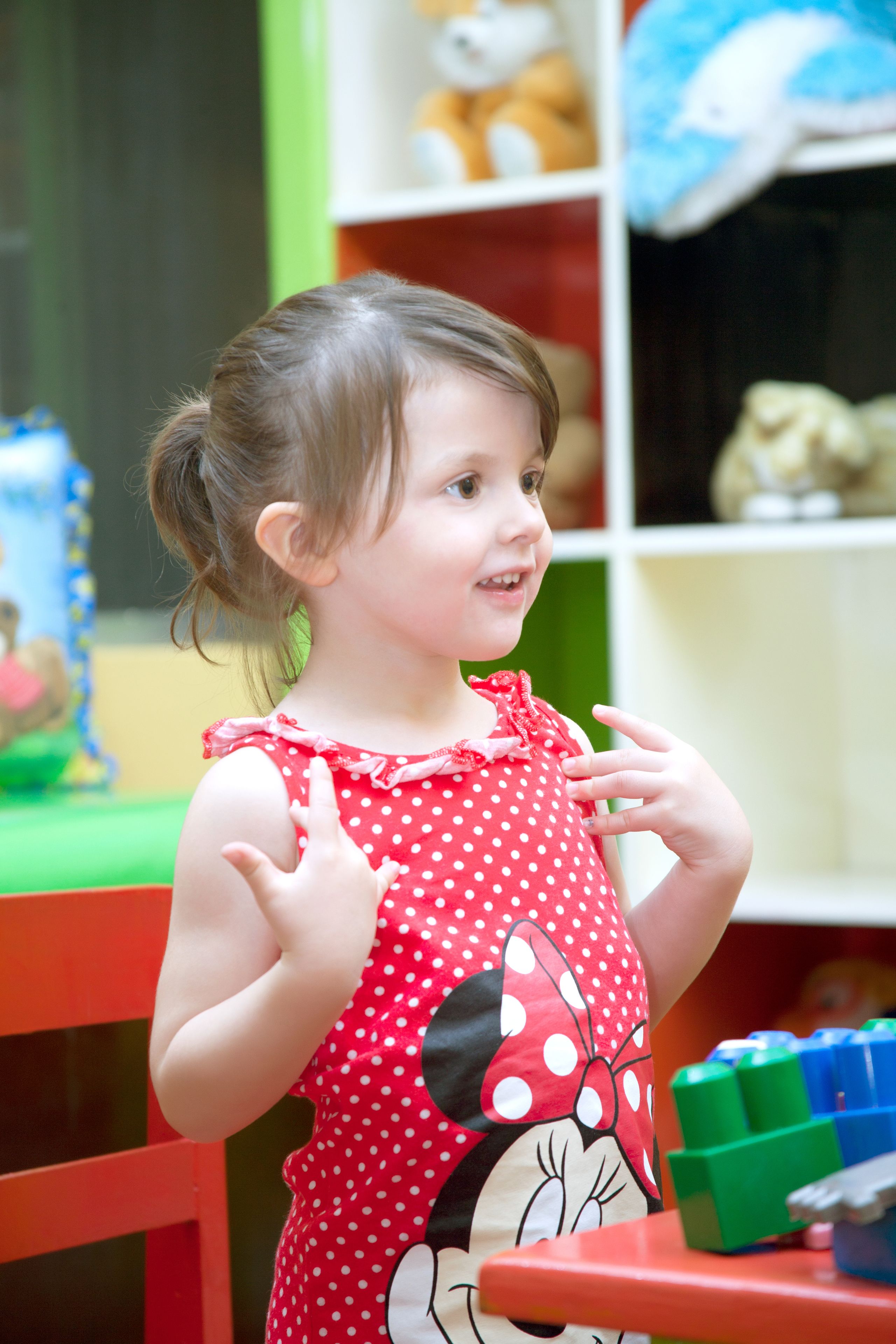 A child in a polka dot dress standing at a table with colorful blocks.