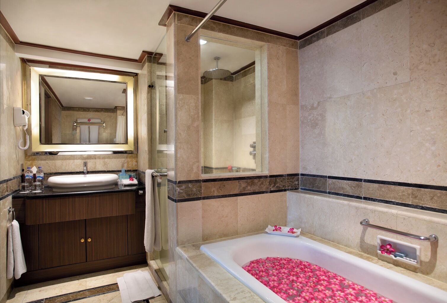 Une salle de bain moderne avec un grand miroir, une baignoire remplie de pétales de roses, un espace douche et un meuble-lavabo avec un évier et un porte-serviettes.