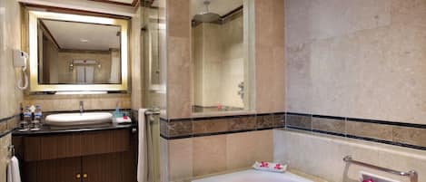 A modern bathroom with a large mirror, a bathtub filled with rose petals, a shower area, and a vanity with a sink and towel rack.