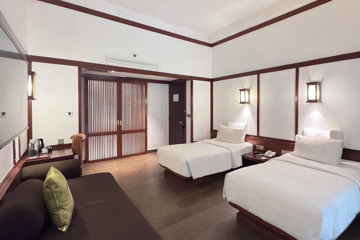 A hotel room with two beds, a sofa, a wooden floor, and a sliding door.