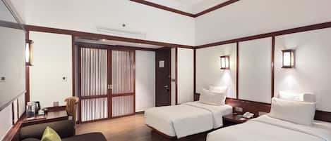 A hotel room with two beds, a sofa, a wooden floor, and a sliding door.
