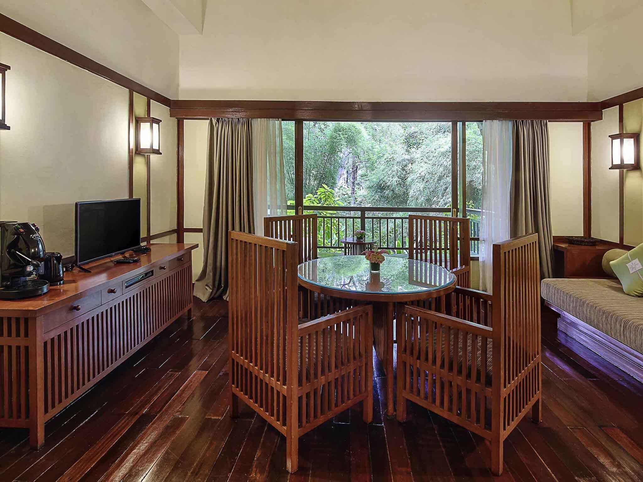 A room with a wooden dining table, chairs, a sofa, a TV, and a coffee maker.