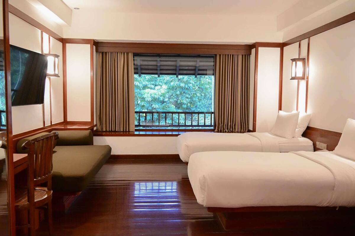 A hotel room with a bed, a sofa, a TV, and a window with curtains.