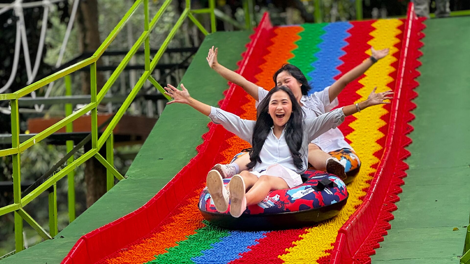 Two people sliding down a colorful slide with a green metal structure.