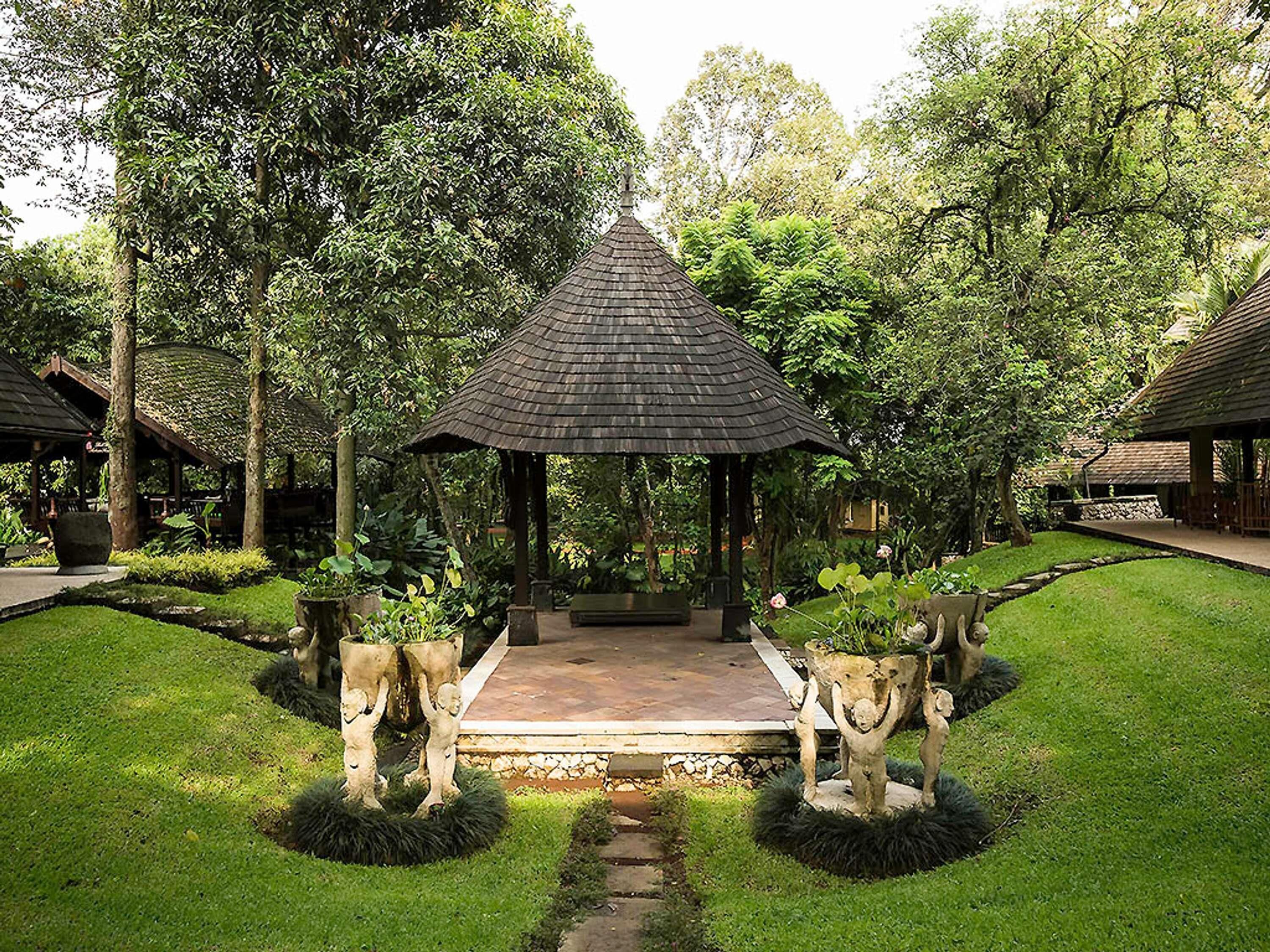 A gazebo surrounded by lush greenery, with a stone pathway leading to it.