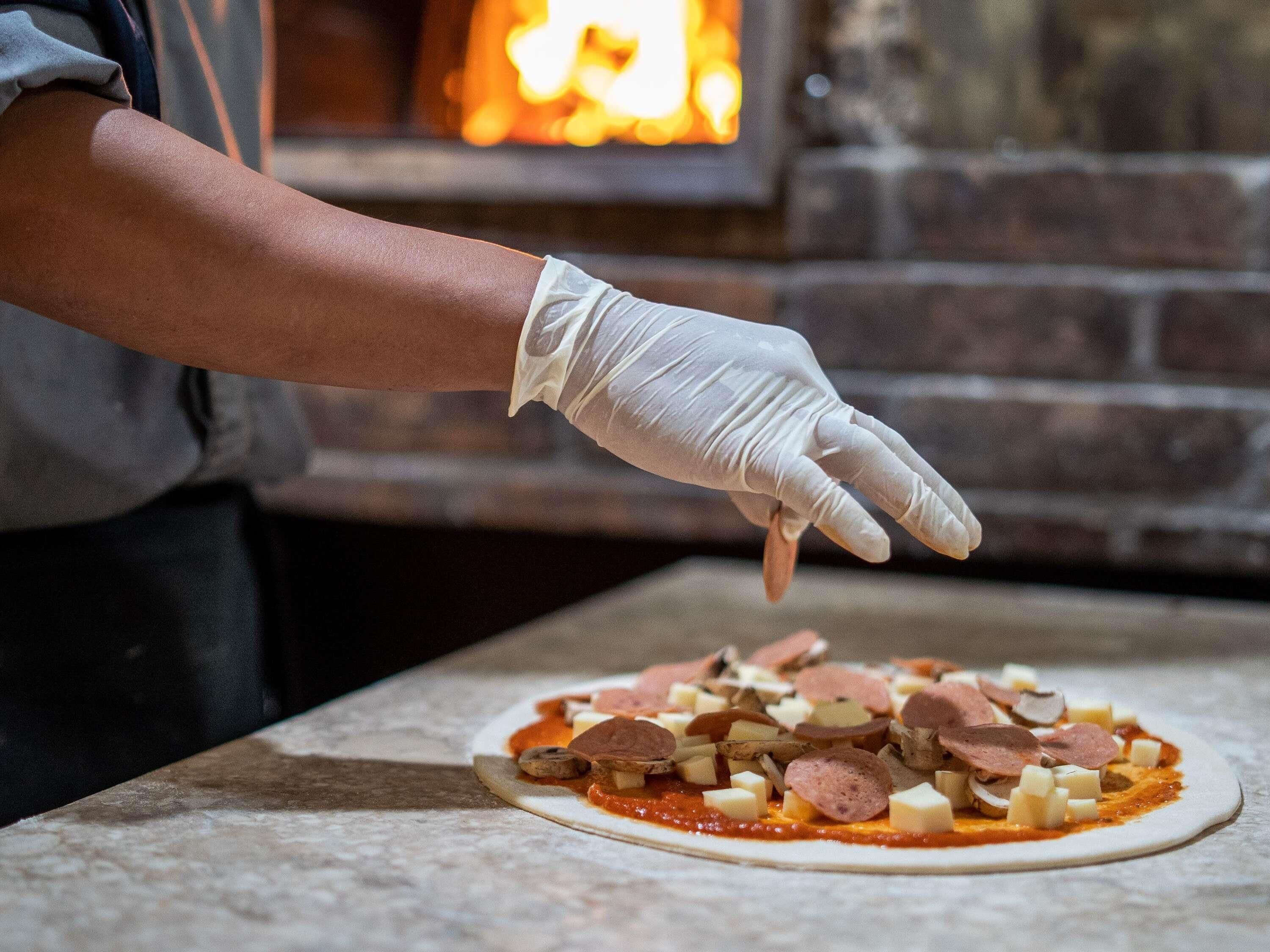 En person laver en pizza med forskellige fyld på en flad overflade.