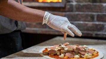 En person laver en pizza med forskellige fyld på en flad overflade.