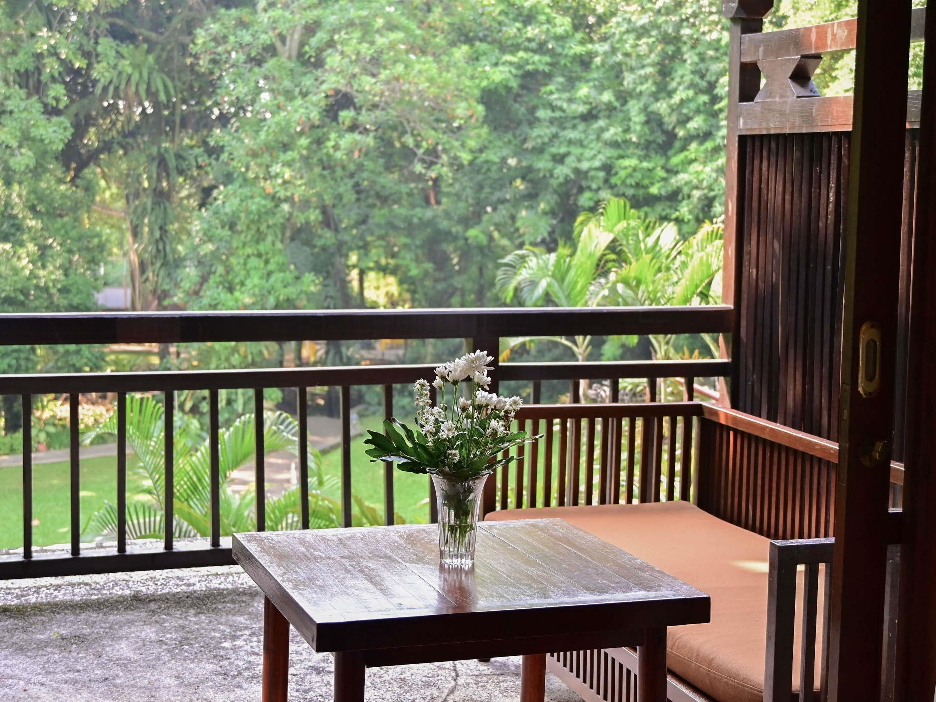 Una mesa de madera con un florero de flores en un balcón con vistas a exuberante follaje.