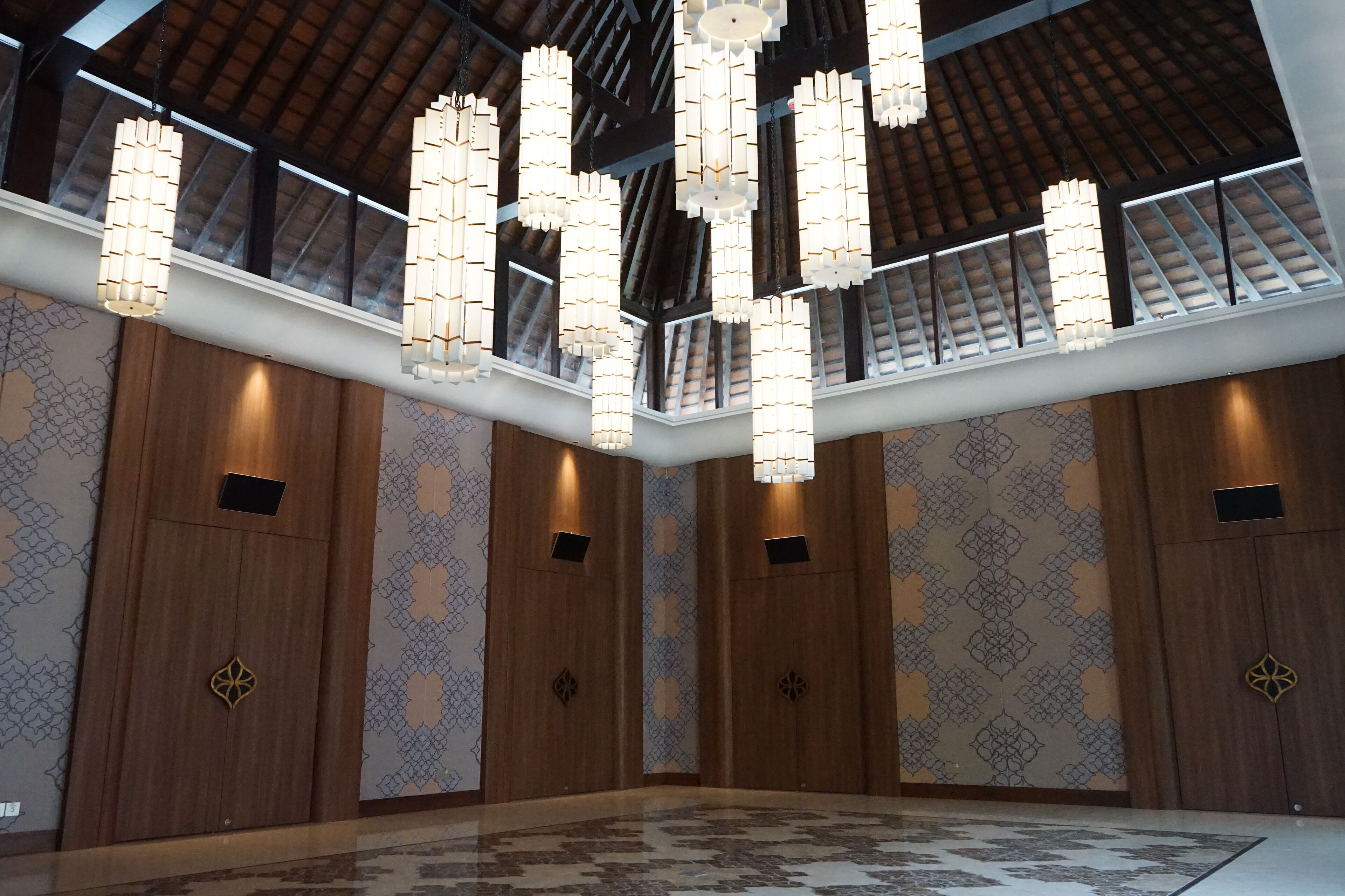 A spacious interior with high ceilings, patterned walls, and multiple hanging light fixtures.