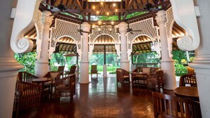 A covered outdoor seating area with wooden furniture and columns, surrounded by greenery. - Novotel Bogor Golf Resort & Convention Center (Bogor)