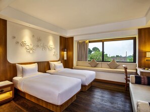 A hotel room with two beds, a sofa, a window with a view, and a wall-mounted light fixture. - Novotel Bogor Golf Resort & Convention Center (Bogor)