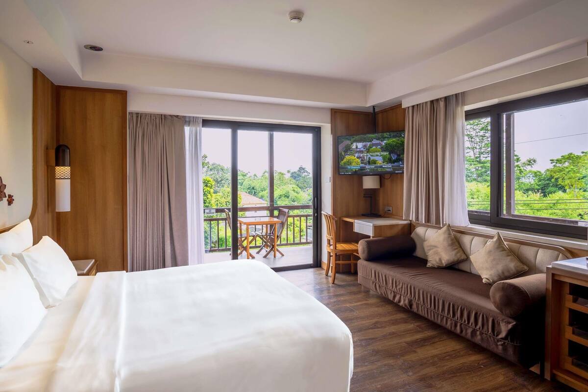 A hotel room with a bed, a sofa, a TV, and a balcony with a view.