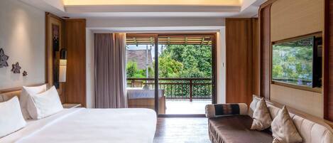 Habitación de hotel con cama, sofá, televisión y balcón con vistas a zonas verdes.