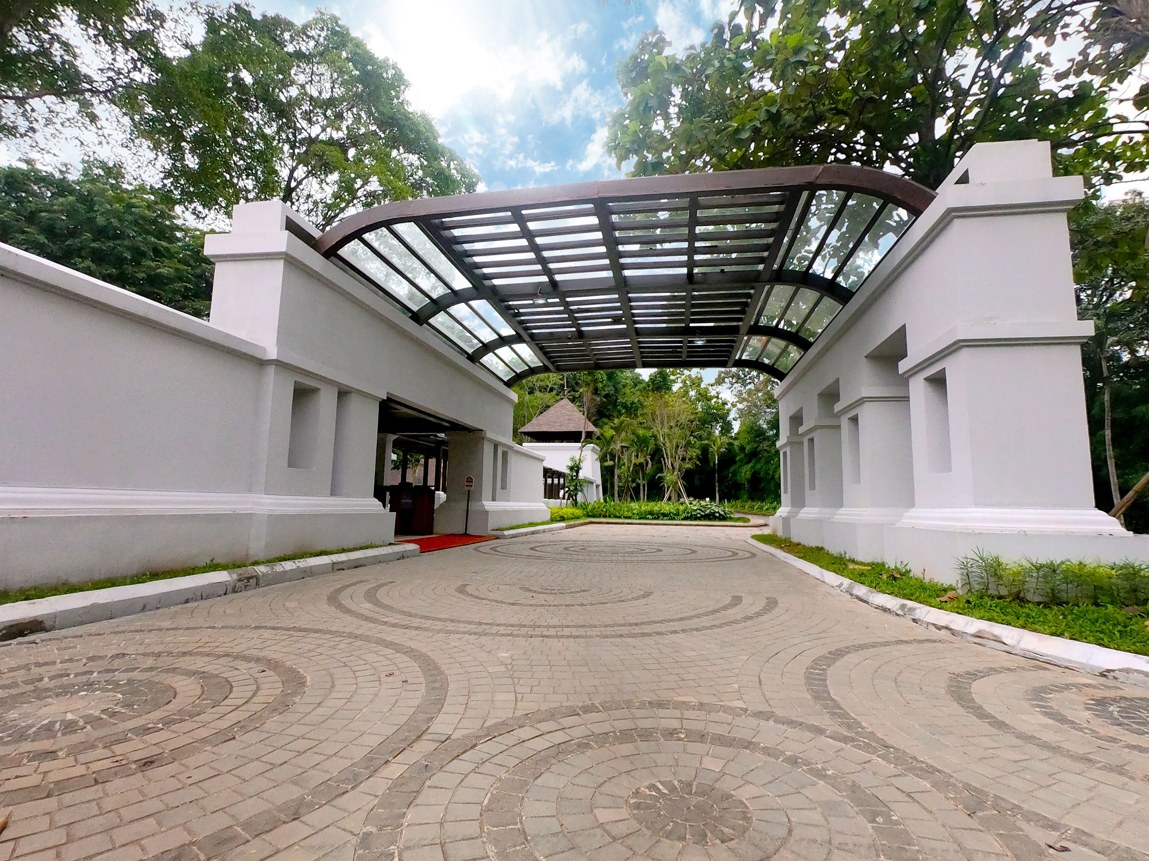 A paved pathway leading to a building with a covered entrance and a red carpet.