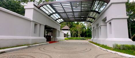 A paved pathway leading to a building with a covered entrance and a red carpet.