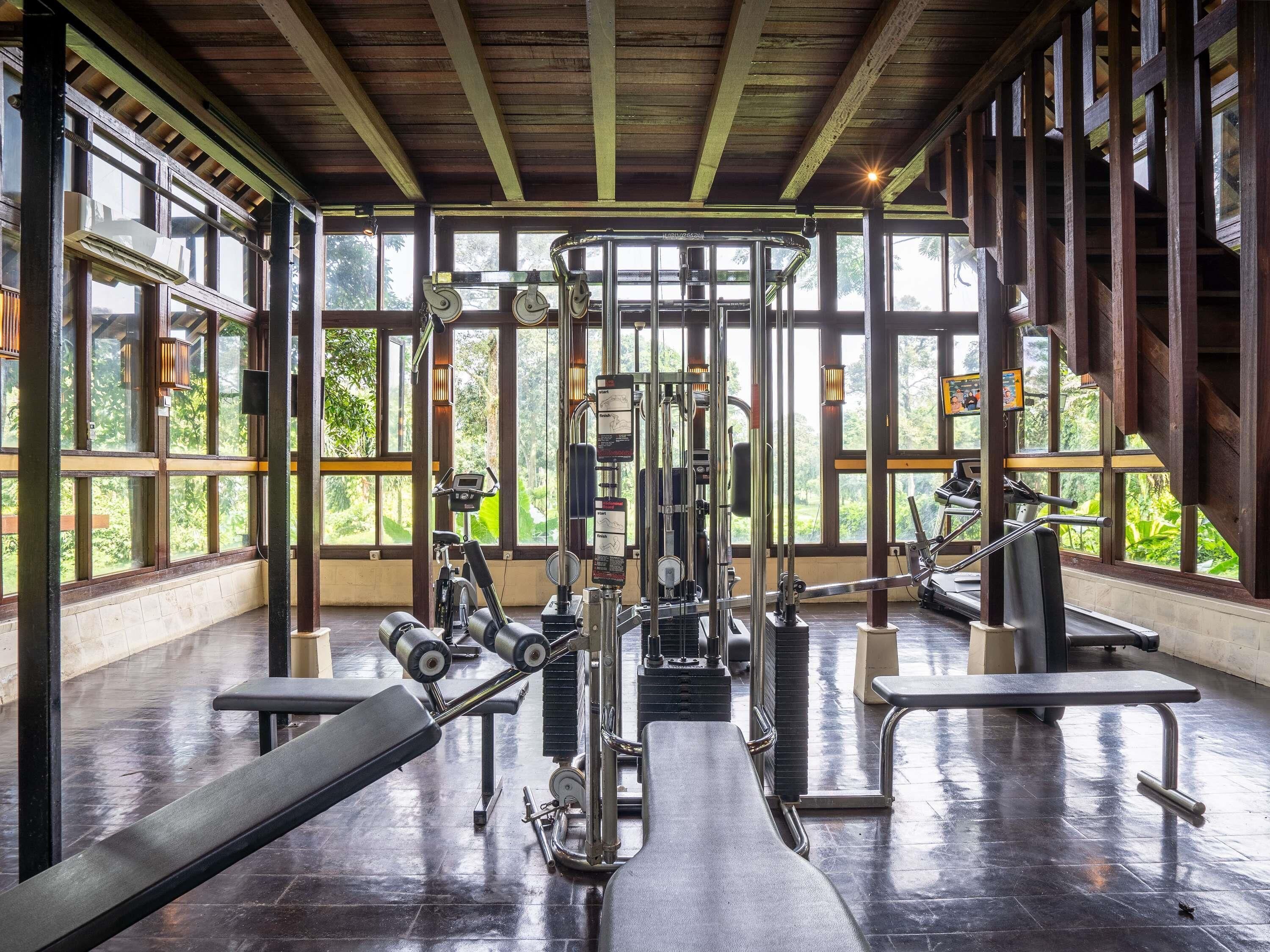 A gym with exercise equipment, large windows, and a wooden ceiling.