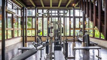 A gym with exercise equipment, large windows, and a wooden ceiling.