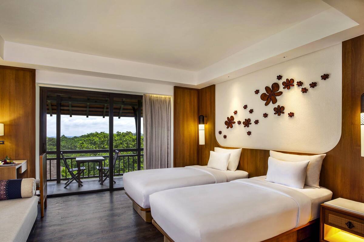 A hotel room with two beds, a balcony with a table and chairs, and a decorative wall with floral patterns.
