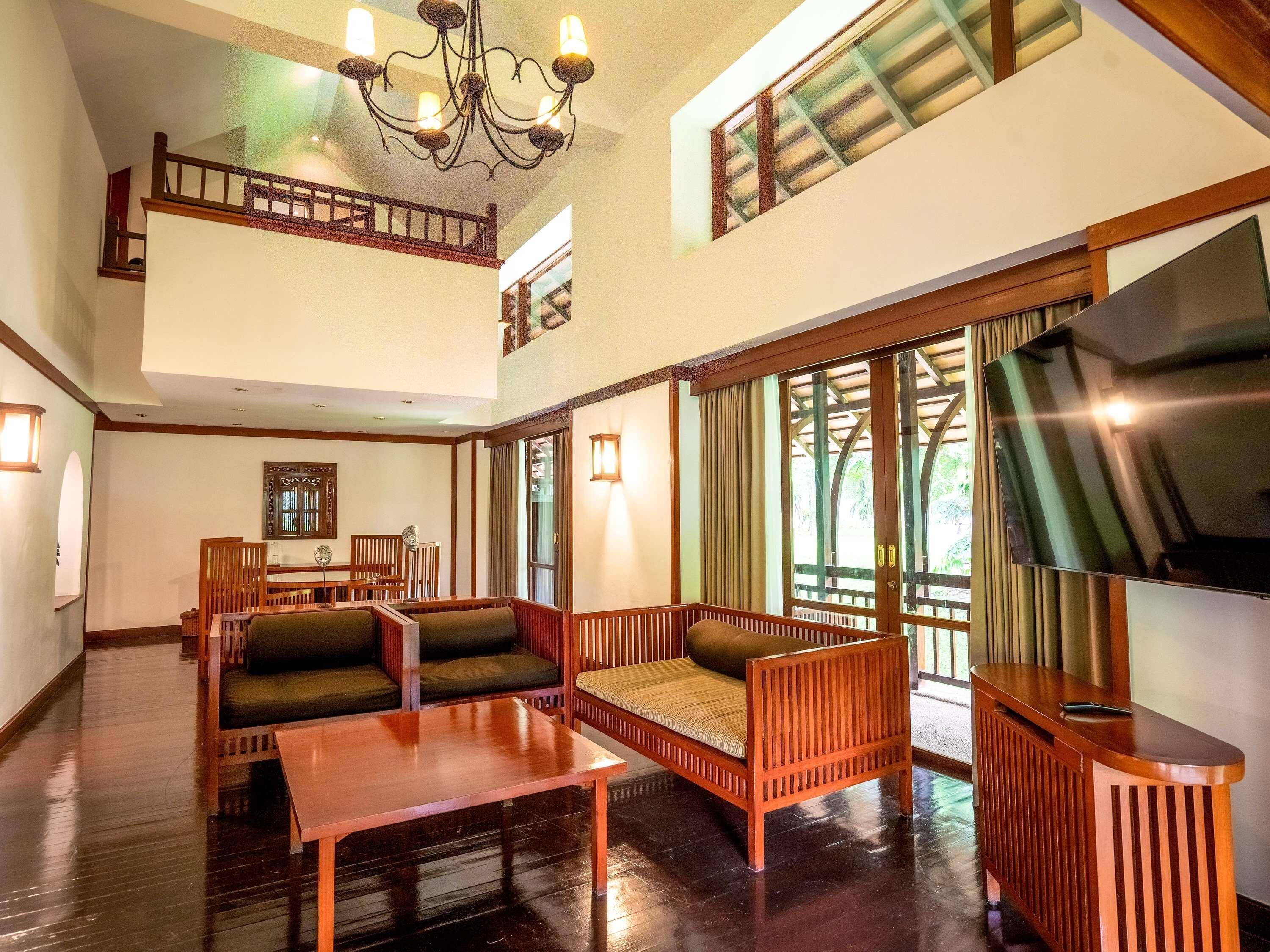 A spacious living area with a wooden sofa set, a coffee table, a TV, and a balcony with a view.