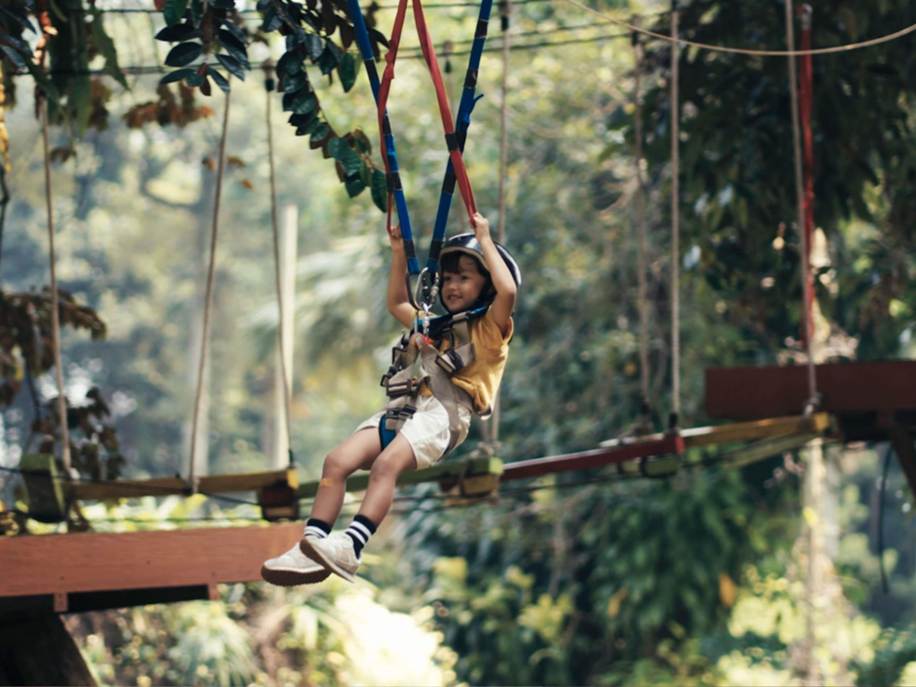 A person zip-lining through a forested area with a safety harness and helmet.