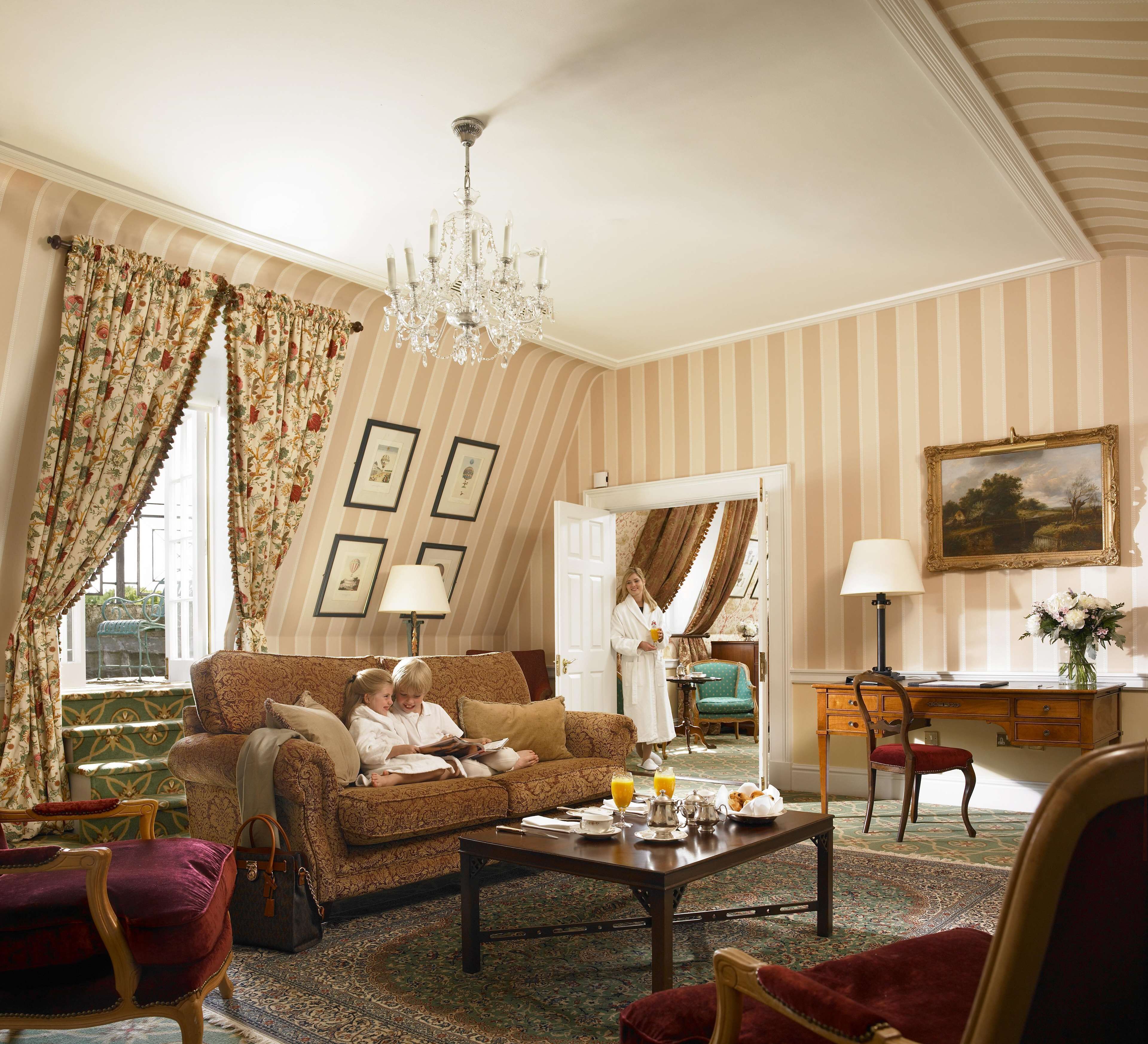 A cozy living room with striped wallpaper, a chandelier, and a dining area with a table set for breakfast.