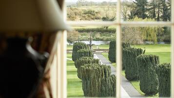 A view through a window of a well-manicured garden with a pond, neatly trimmed hedges, and a statue.