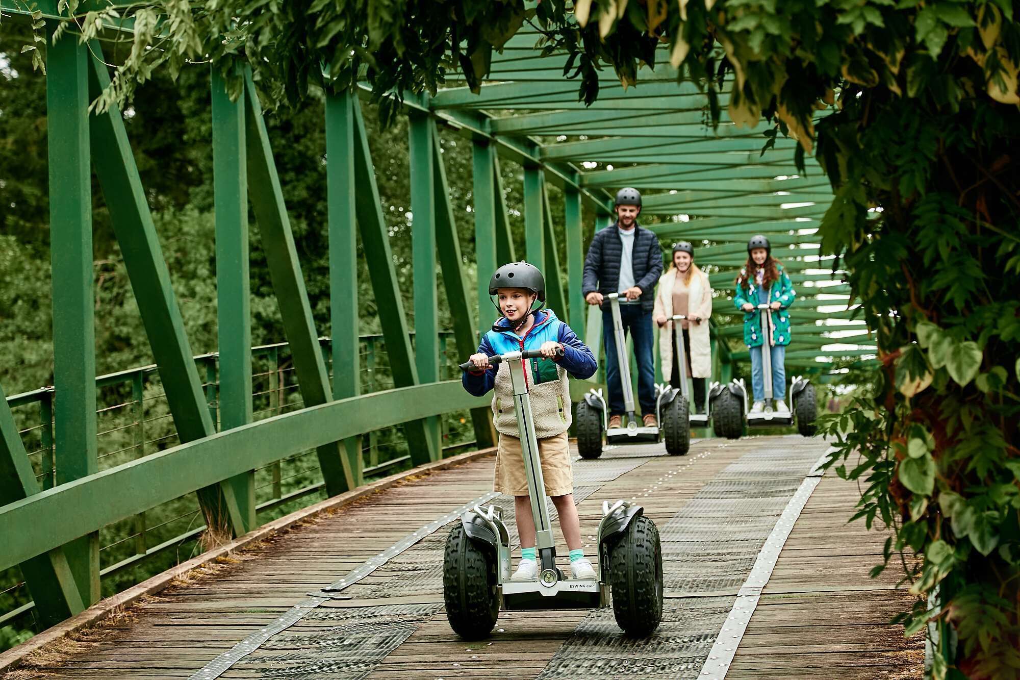 A person riding a Segway on a wooden bridge with metal railings, surrounded by greenery.