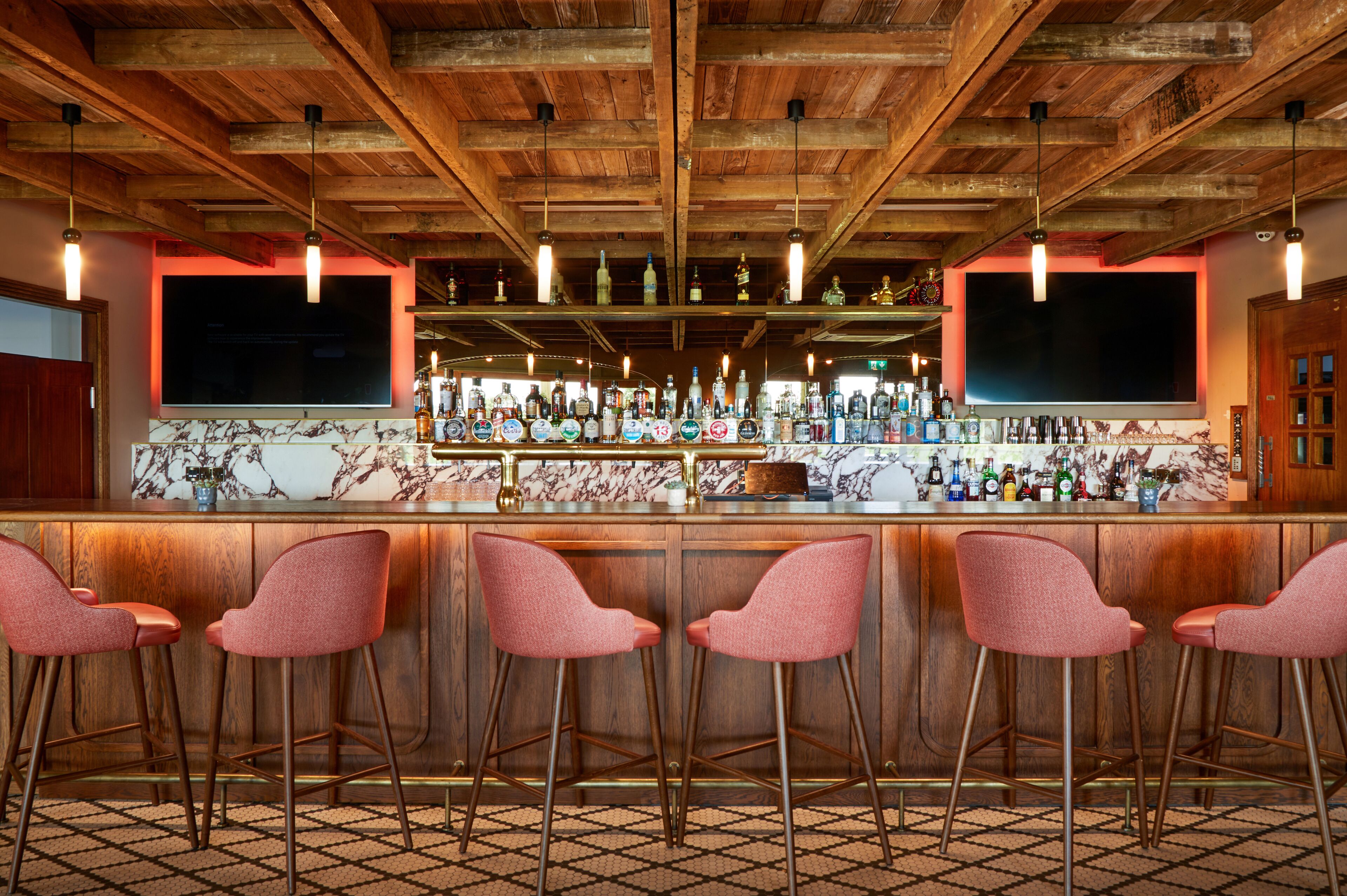 A bar area with wooden ceiling beams, a marble countertop, and four pink bar stools.
